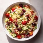 Greek Orzo Salad in a white bowl with cherry tomatoes, cucumbers, olives, and feta