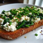 A close-up of a delicious Cottage Cheese and Spinach Breakfast Toast topped with chives and chili flakes on a white plate.