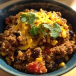 A close-up of a bowl of One Pot Mexican Beef Quinoa, topped with shredded cheddar cheese and fresh cilantro.