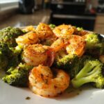 A close-up shot of a white plate filled with perfectly cooked Sheet Pan Shrimp and Broccoli, seasoned with herbs and spices.