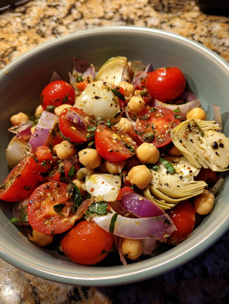 A close-up of a vibrant Artichoke Tomato Chickpea Salad in a light blue bowl, featuring cherry tomatoes, chickpeas, artichoke hearts, and red onion.