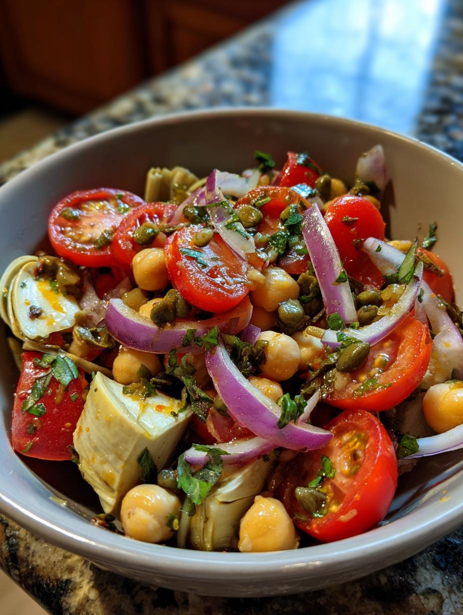 A vibrant bowl of Artichoke Tomato Chickpea Salad with red onion and capers, garnished with fresh parsley.