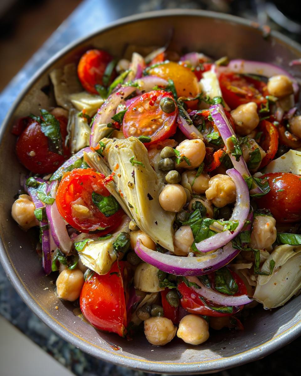 Close-up of a vibrant Artichoke Tomato Chickpea Salad with cherry tomatoes, chickpeas, artichoke hearts, red onion, and capers.