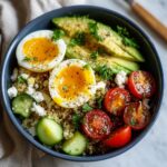 A vibrant Avocado Egg Breakfast Bowl featuring quinoa, soft-boiled eggs, sliced avocado, cherry tomatoes, cucumber, and feta cheese.