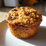 A close-up of a golden-brown Banana Oatmeal Protein Muffin with a textured, crumbly top.