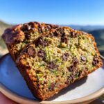 Close-up of two slices of moist chocolate chip zucchini bread on a plate, showcasing the zucchini shreds and melted chocolate chips.
