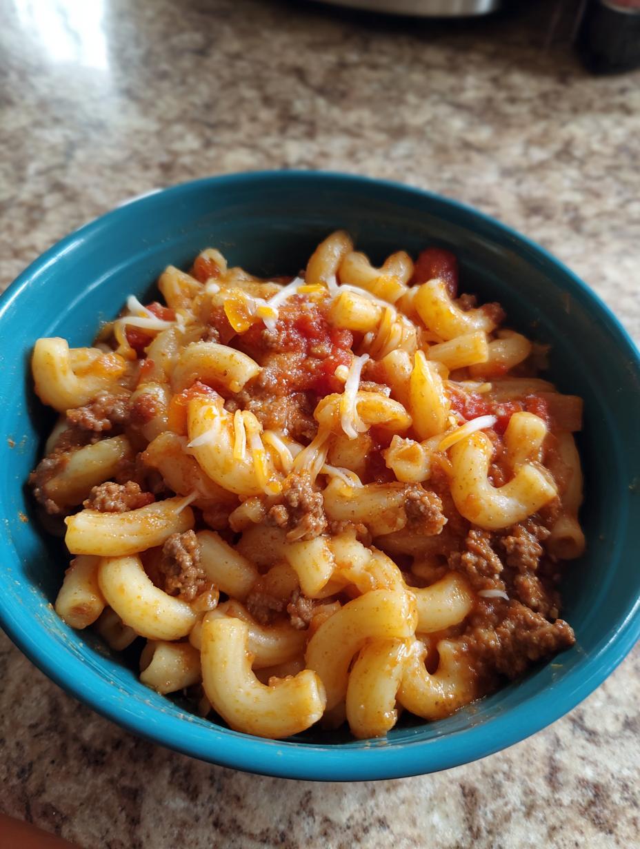 A close-up of a bowl of Classic American Goulash with Macaroni, topped with melted cheese.