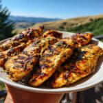 A plate of juicy grilled chicken tenders coated in an easy chicken marinade, with grill marks and herbs.