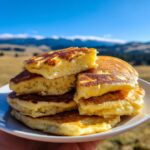 A stack of fluffy Easy Cottage Cheese Pancakes on a white plate, with a bite taken out of the top pancake.