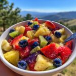 A close-up of a vibrant fruit salad with strawberries, blueberries, kiwi, and pineapple, coated in a glistening honey lime dressing.