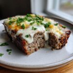 A slice of Garlic Parmesan Meatloaf with Creamy Sauce, topped with melted cheese and parsley, on a plate.