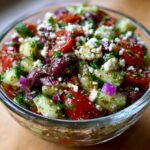 A close-up of Greek Style Tomato Cucumber Salsa in a glass bowl, featuring chopped tomatoes, cucumbers, olives, feta cheese, and red onion.
