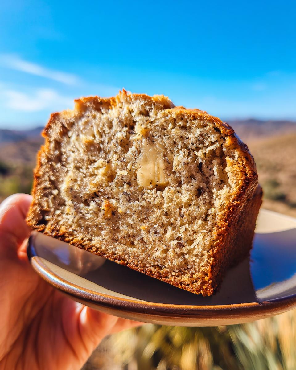 A slice of moist Greek yogurt banana bread held on a plate, with visible banana chunks and a golden crust.