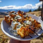 A plate of juicy grilled chicken skewers generously drizzled with creamy yogurt sauce and herbs.