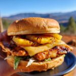 A close-up of a delicious Hawaiian chicken sandwich featuring grilled chicken, melted cheese, and grilled pineapple slices on a bun.