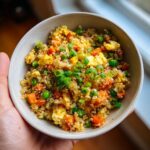 A close-up of a bowl filled with Healthy Cauliflower Fried Rice, featuring scrambled eggs, peas, carrots, and green onions.