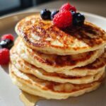 A stack of fluffy Healthy Cottage Cheese Pancakes topped with fresh raspberries and blueberries, drizzled with syrup.