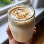 Close-up of a healthy peanut butter banana smoothie in a glass jar, topped with a swirl of peanut butter.