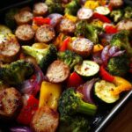 Close-up of a sheet pan filled with Healthy Sheet Pan Sausage and Veggies, including broccoli, bell peppers, zucchini, and red onion.