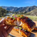 Close-up of a flaky, moist piece of honey glazed salmon, garnished with green onions and zest.