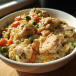 Close-up of a bowl filled with Instant Pot Creamy Chicken and Rice, featuring tender chicken pieces, fluffy rice, peas, and carrots.
