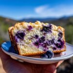 A slice of Lemon Blueberry Bread Perfect, showcasing plump blueberries and a crumbly topping, held on a plate.