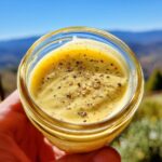 Close-up of a jar filled with creamy Lemon Vinaigrette Dressing, topped with cracked black pepper.