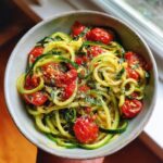 A bowl of light zucchini noodles tossed with cherry tomatoes and fresh basil, sprinkled with parmesan cheese.