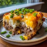 A delicious slice of Loaded Potato Meatloaf Casserole, topped with melted cheese and green onions.