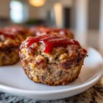 Close-up of a Mini Meatloaf Muffin topped with ketchup, served on a white plate.