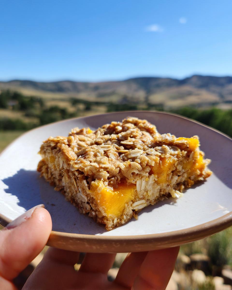 A slice of Peach Baked Oatmeal Easy Summer Breakfast Recipe on a plate with a scenic outdoor background.
