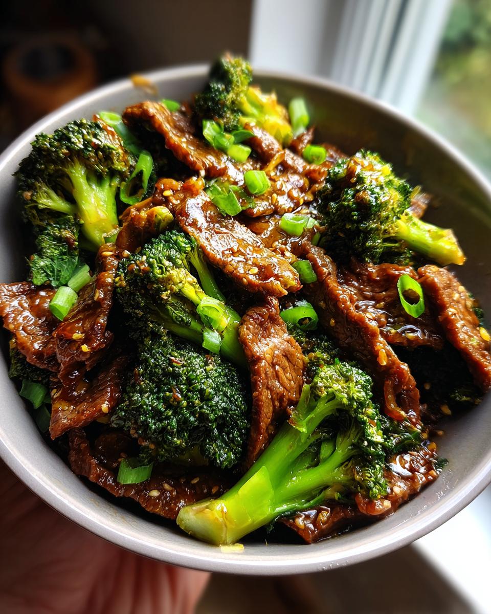 A close-up of a bowl filled with Quick Healthy Beef and Broccoli Stir Fry, garnished with green onions and sesame seeds.