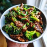 A bowl of Quick Healthy Beef and Broccoli Stir Fry, glistening with sauce and topped with sesame seeds and green onions.