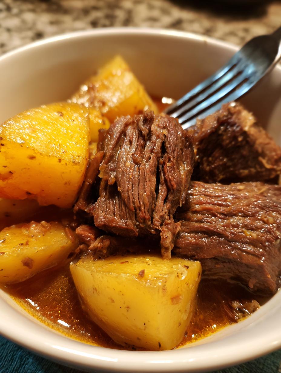 Close-up of tender Slow Cooker Chuck Roast and Potatoes in a white bowl with a fork.