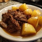 A bowl of tender slow cooker chuck roast and potatoes in a rich gravy.