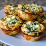 A plate of golden-brown Spinach and Feta Egg White Muffins, topped with crumbled feta cheese and visible spinach.