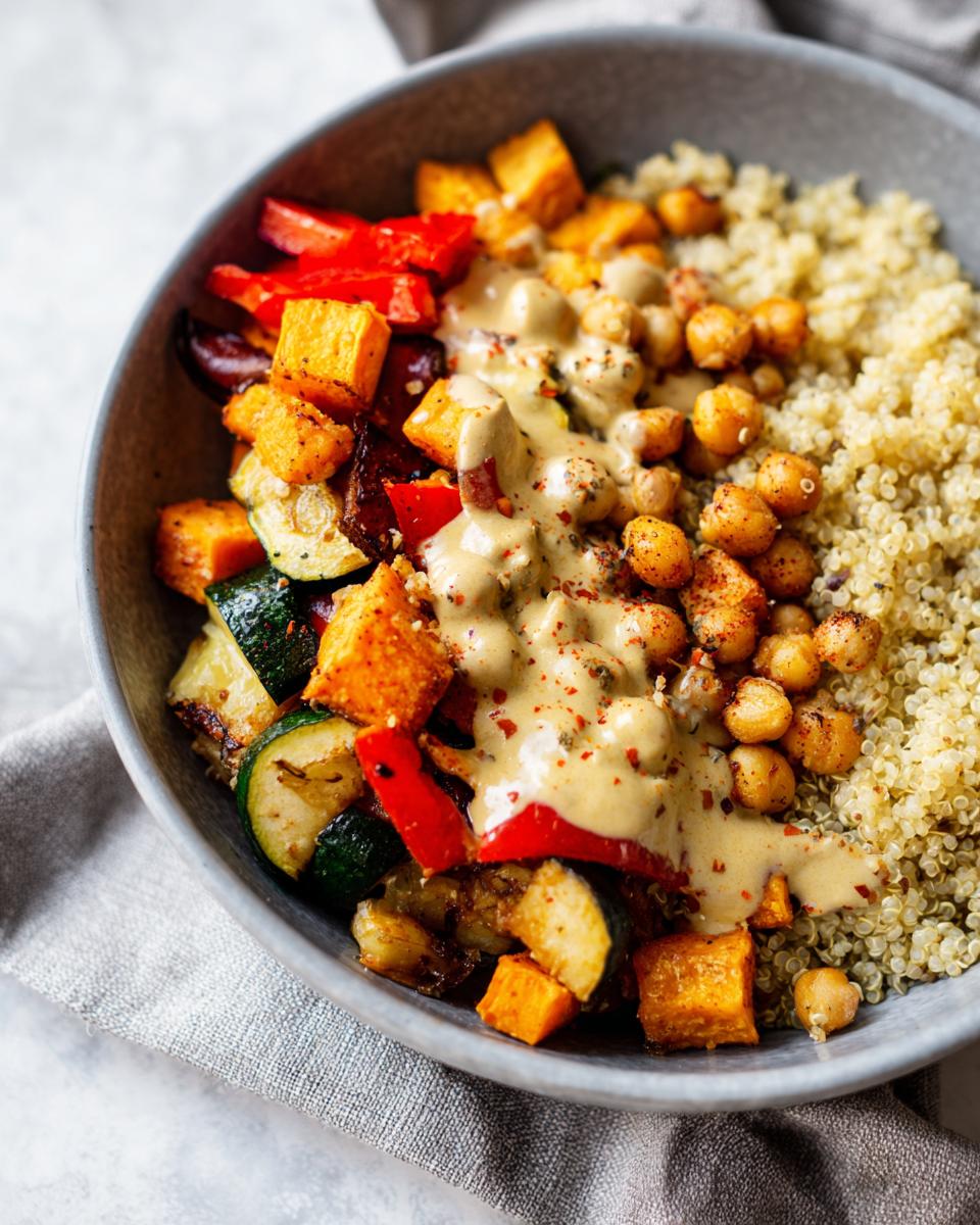 A close-up of a Vegan Chickpea and Quinoa Meal Prep Bowl filled with roasted vegetables, chickpeas, and quinoa, drizzled with tahini dressing.