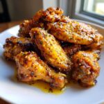 A close-up of a pile of glistening Wet Lemon Pepper Wings, coated in a savory sauce and sprinkled with herbs.