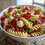 A bowl of Zesty Italian Pasta Salad featuring rotini pasta, salami, cherry tomatoes, mozzarella balls, olives, and green peppers.