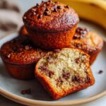 A close-up of guilt-free banana protein muffins, one sliced to show chocolate chips and moist interior.