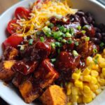 Close-up of a bowl filled with BBQ chicken sweet potato bowls, featuring chicken, sweet potatoes, corn, black beans, tomatoes, and cheese.