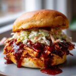 A close-up of a delicious bbq pulled chicken sandwich piled high with coleslaw and dripping with sauce.