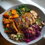 A close-up of a bowl filled with blackened chicken and sweet potato, quinoa, kale, and red cabbage.