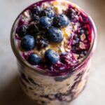 Close-up of blueberry lemon overnight oats in a glass jar, topped with fresh blueberries and a swirl of blueberry compote.