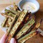 Hand holding a pile of crispy cajun roasted okra fries, with a bowl of dipping sauce in the background.