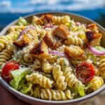 A close-up of a bowl of Chicken Caesar Pasta Salad with fusilli pasta, grilled chicken, croutons, and cherry tomatoes.