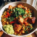A bowl of chicken taco rice skillet topped with jalapeños, cilantro, and red bell peppers, with a side of guacamole.