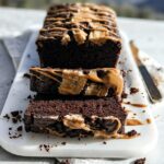 Close-up of moist chocolate peanut butter banana bread, drizzled with peanut butter and topped with banana slices.