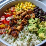 A close-up of a vibrant cilantro lime rice bowl filled with seasoned chicken, black beans, corn, tomatoes, and avocado.