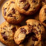 A close-up view of tender cottage cheese chocolate chip cookies, with one cookie broken in half to reveal a gooey center.